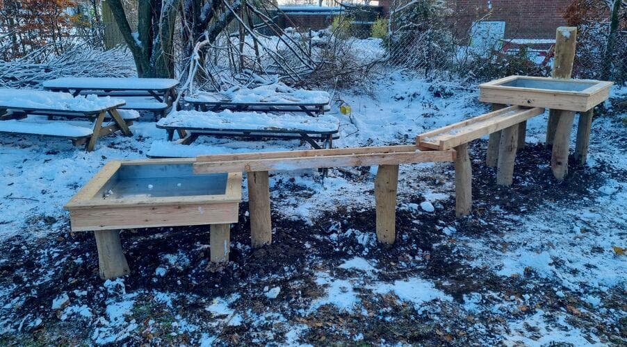 To sandetabeller i træ med indbyggede sandsandkasser på snedækket terrain
