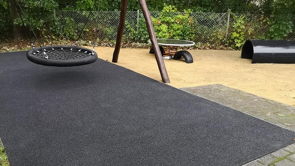 Legeområde med sort gummiunderlag, dækudspring og redskaber på sandbund