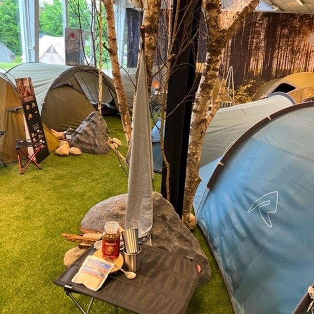 Campingsted med telte, kunstgræsunderlag og træer omkring opstillingsarealet