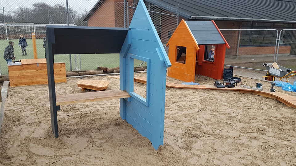 Legehuler i træ med blåt og orange-rødt tag på sandunderlag