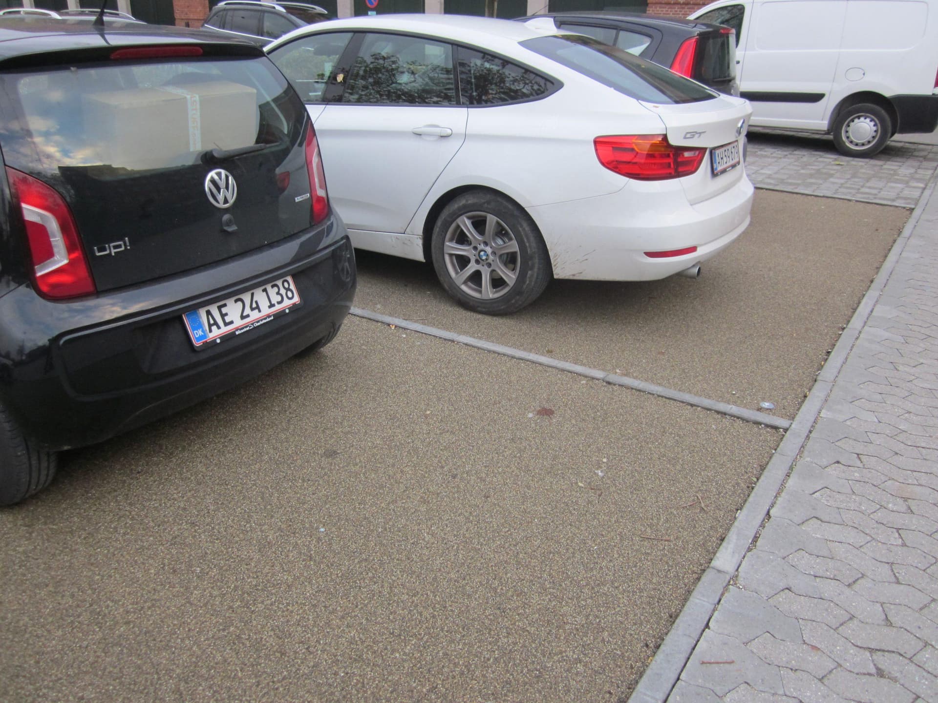 Parkeret sort og hvid bil på befæstet parkeringsplads med græsfliser