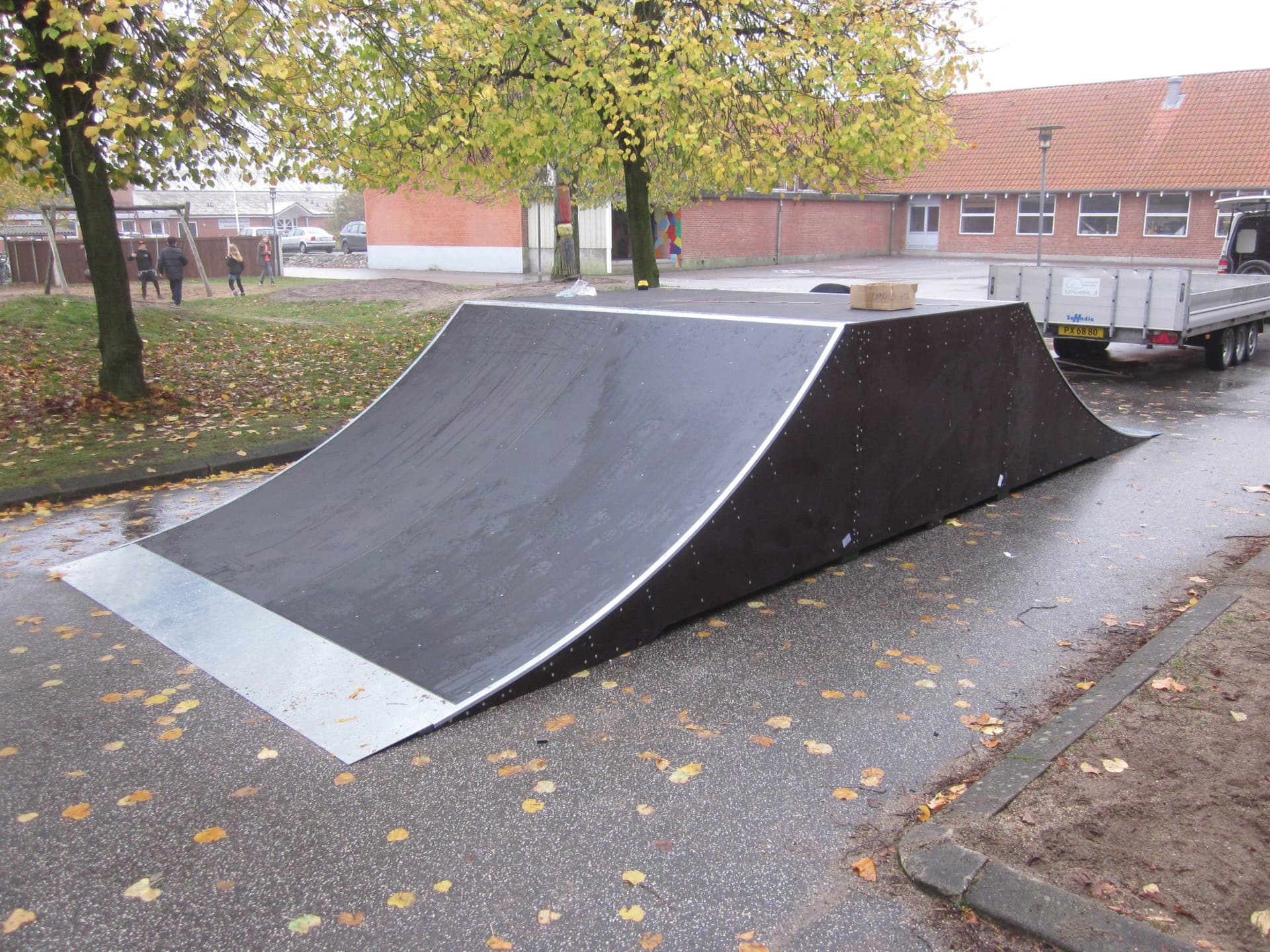 Sort skateboard-rampe med hvid kant på asfaltvej ved skole