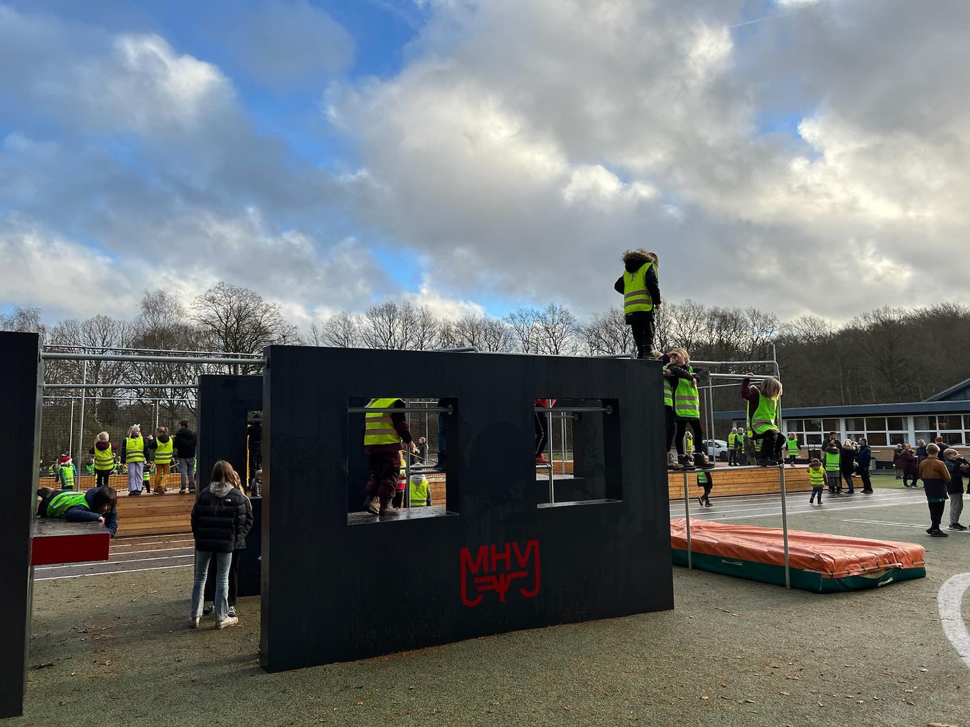 Børn og voksne ved sort eventcontainer og rødt springunderlag på åbent område