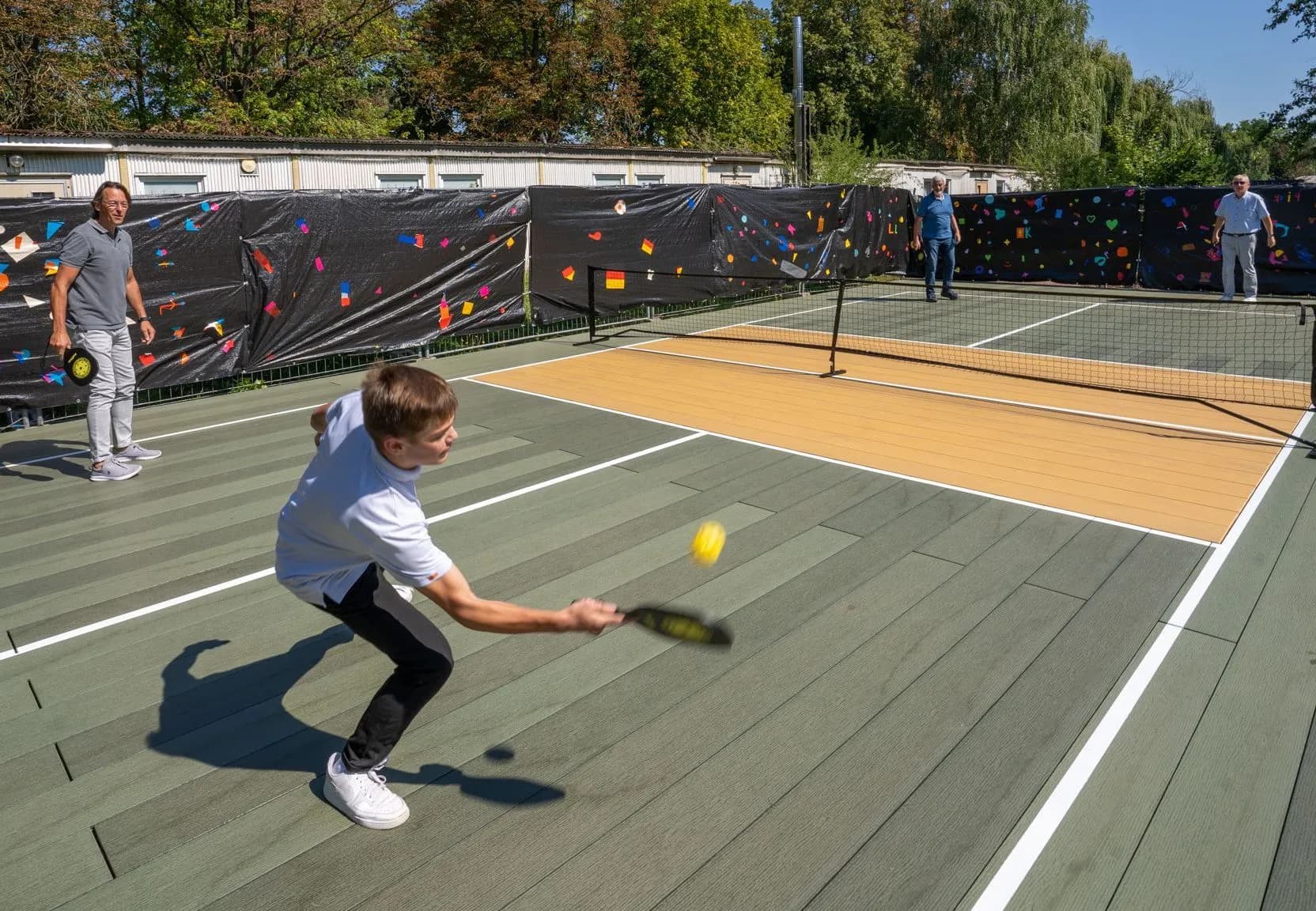Barn spiller paddeltennis på gummikort med net på sportspladsen