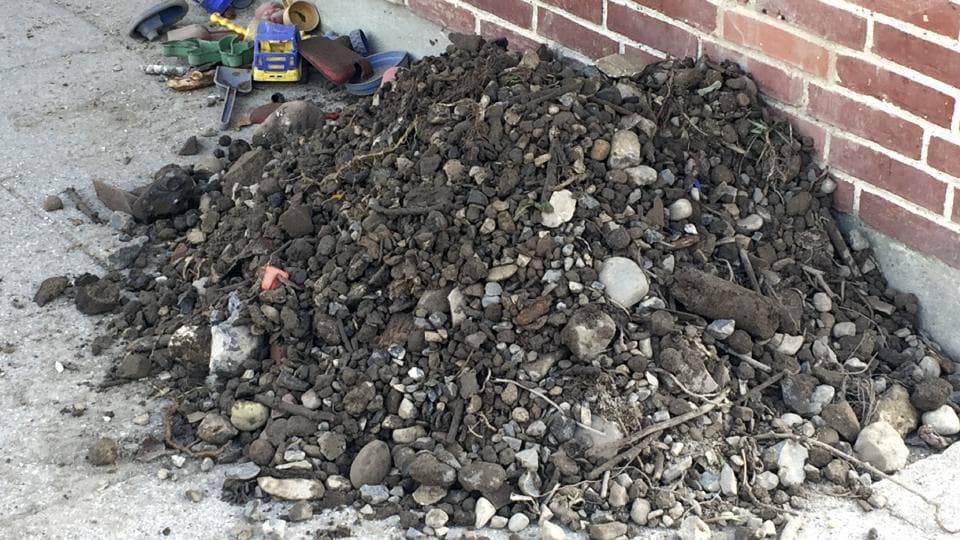 Knust beton og sten på jordanlæg ved muret mur