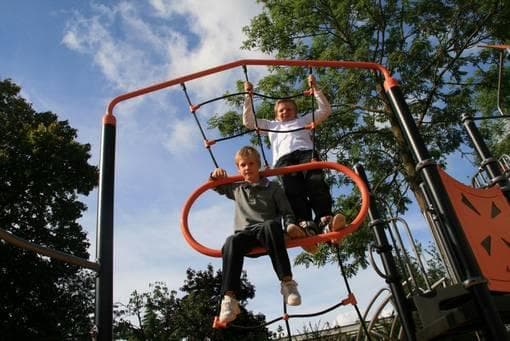 Børn på klatrestativ med røde metalrammer og stiger, træer omkring