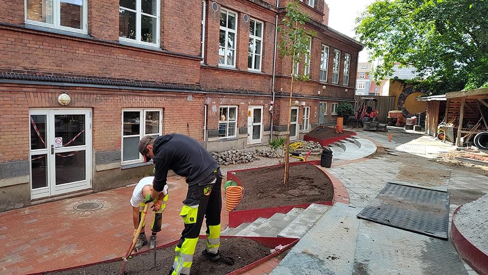 Voksen i højsynlig vest komprimerer rødt faldunderlag på skolegang med tegsten og betonfliser
