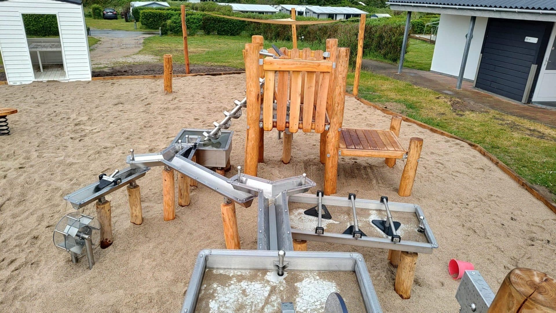 Legeværktøj af metal og træ på sandunderlag med klatrestrukturer og gynger
