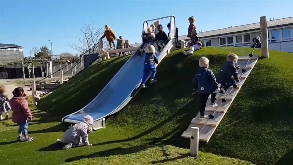 Legebakke med blå rutsjebane, trappe og græsunderlag, børn i leg