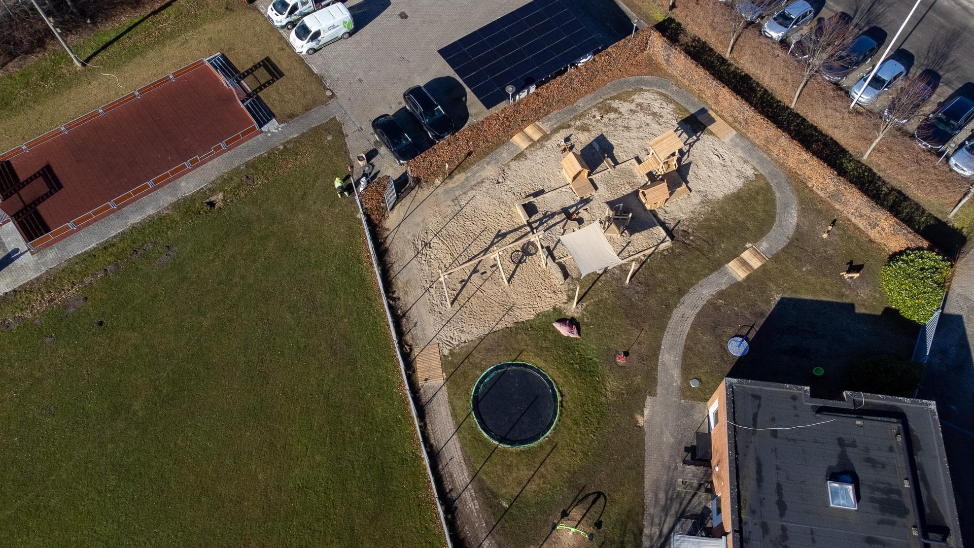 Legeplads med klatrestativer, stige og sandfald set fra oven