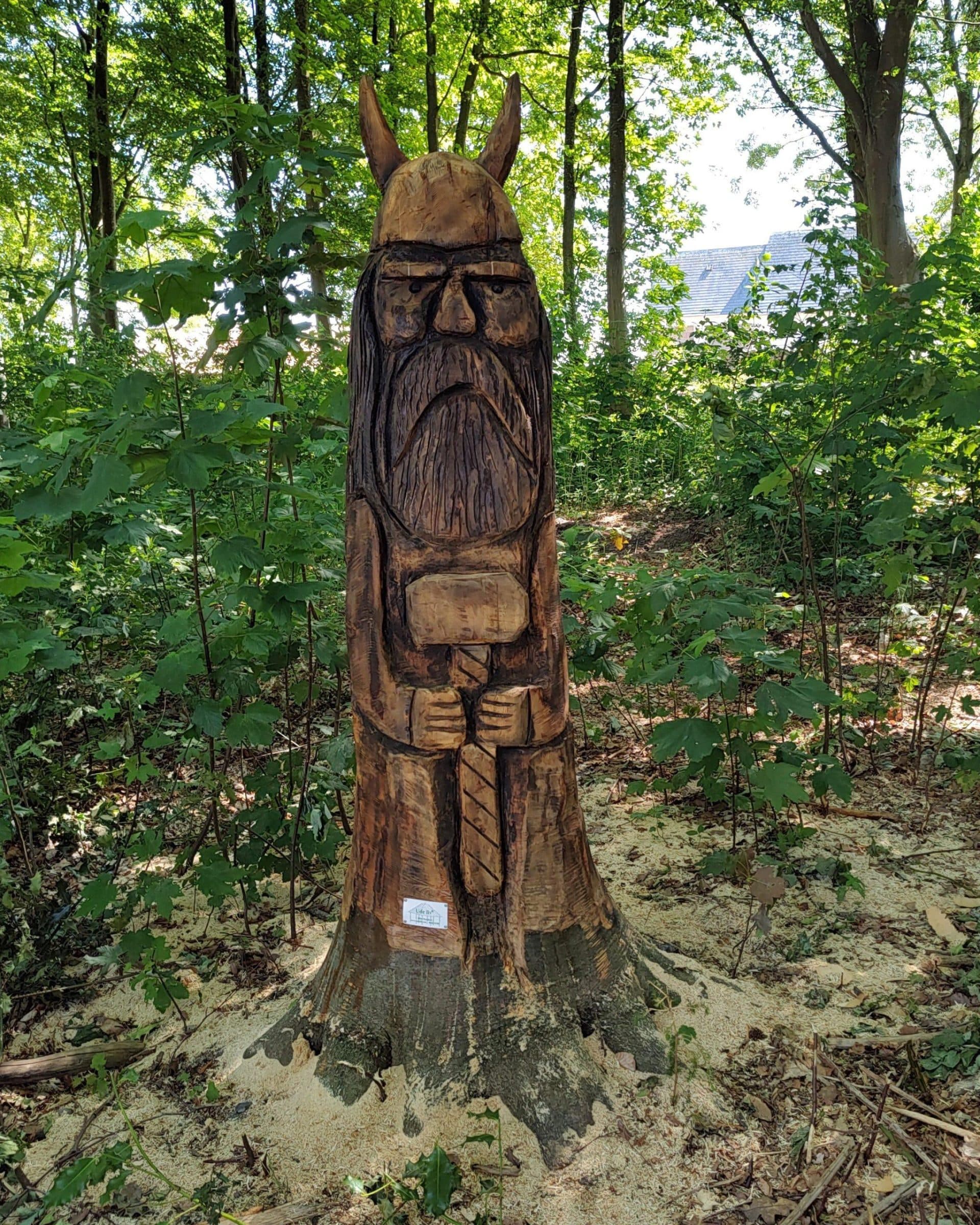 Træskulptur af skægmand udskåret i træstamme blandt skovtræer