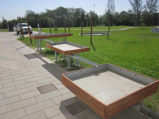 Sandboksæ med træbrætter på flisebelægning ved græsarea med træer