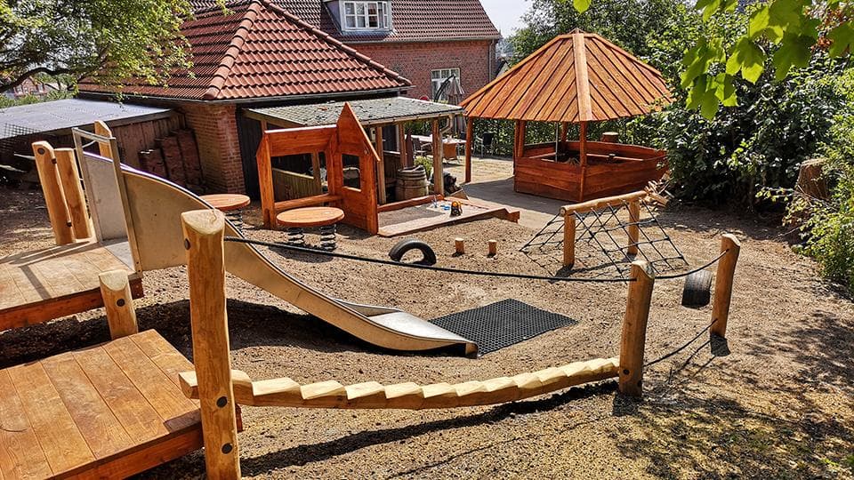 Legeplads med træredskaber, sandunderlag, baldakiner og grønne omgivelser