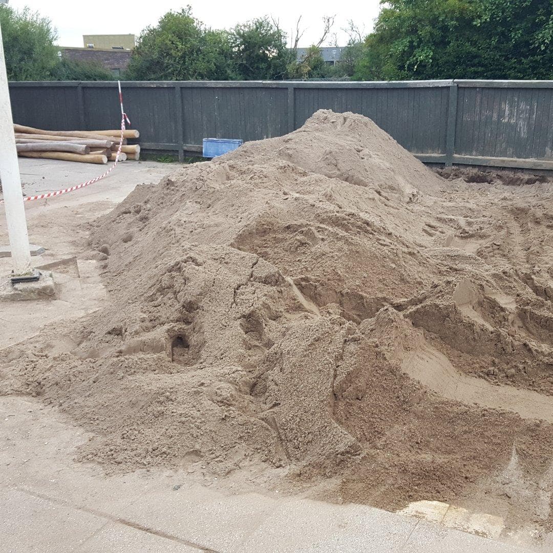 Sandhauge på legeplandsanlæg under opbygning, omgivet af grå hegn