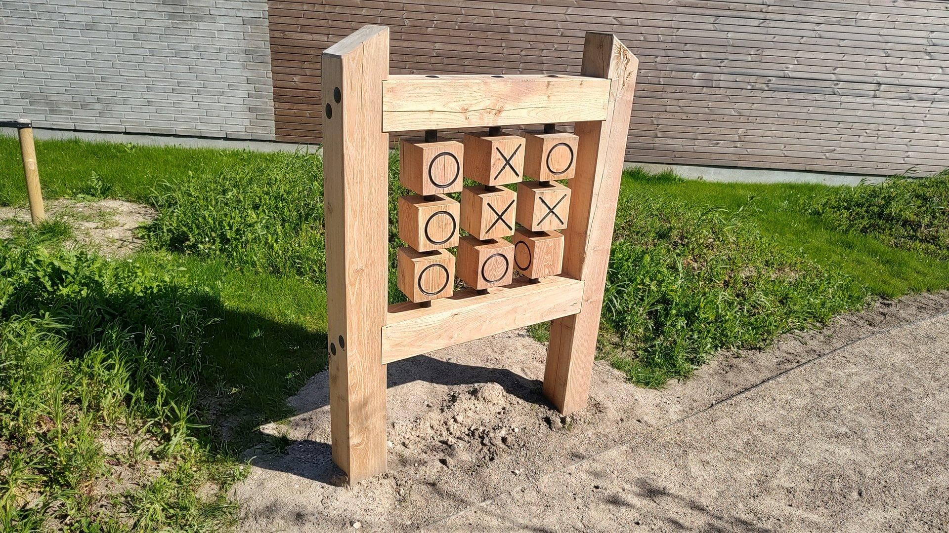 Tre-i-rad-spil i robinietræ på sandunderlag med bygning i baggrunden