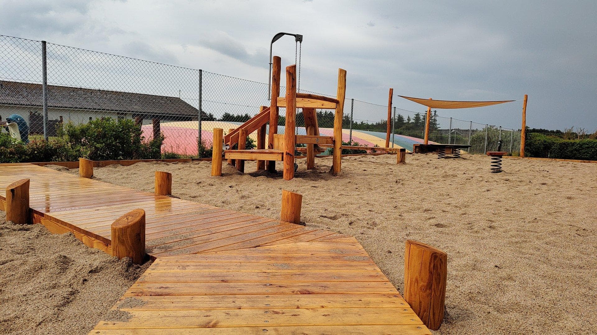 Legeplads med klatretårn i træ, gynger og sandfald på sand med træ-platforme og stolper