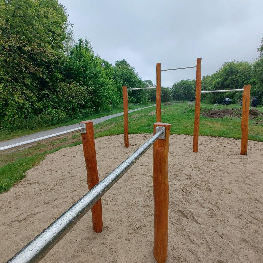 Balancestokke af træ og metal på sandflade omkranset af græsområde og grønne buske