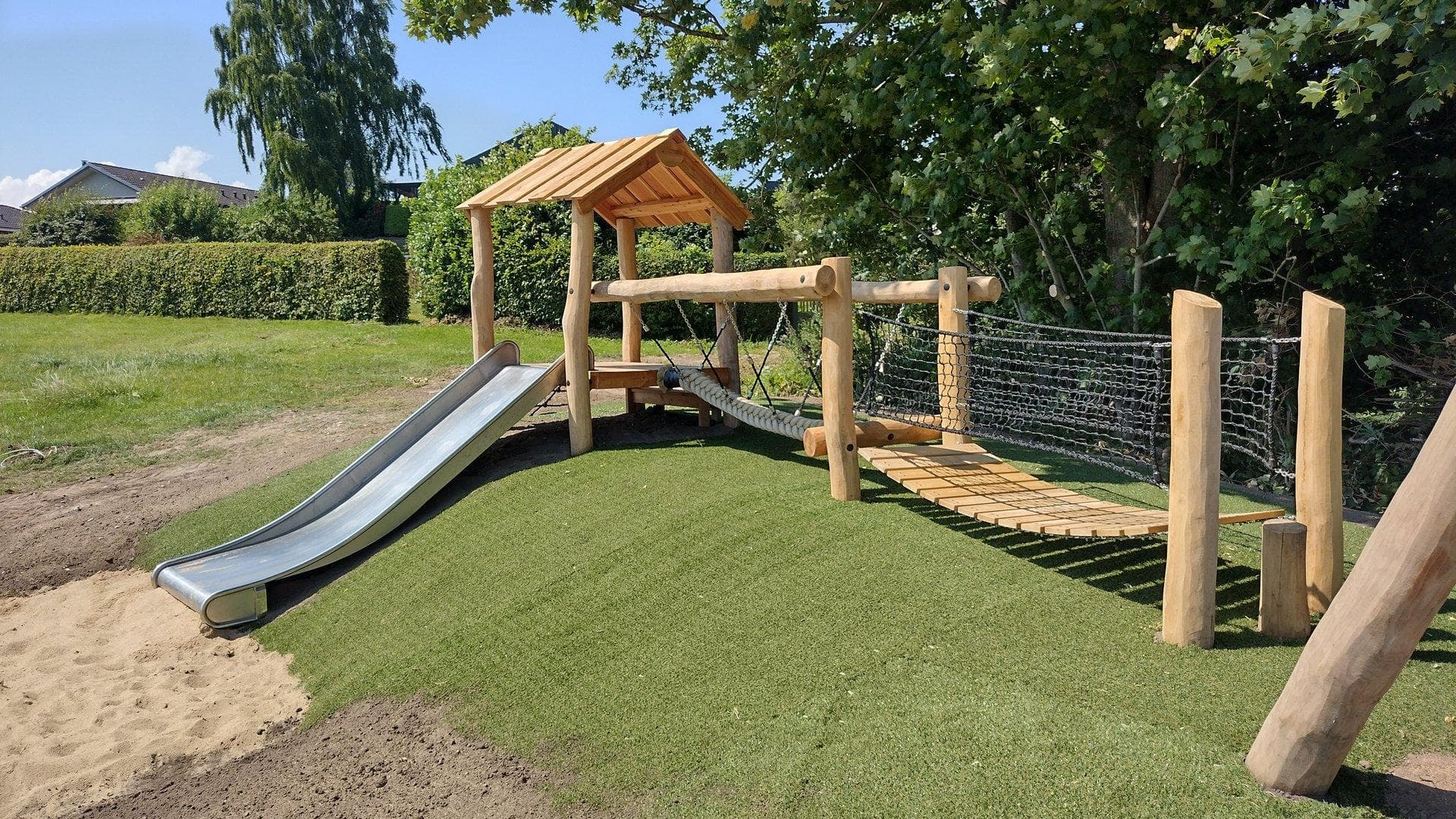 Rutsjebane i rustfrit stål på legeplads med træ-konstruktion og kunstgræs