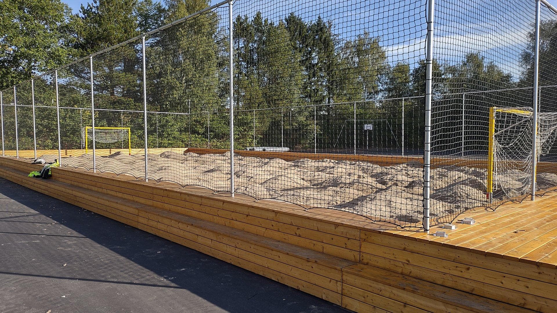 Beachvolleybane med sand og højt hegn under etablering