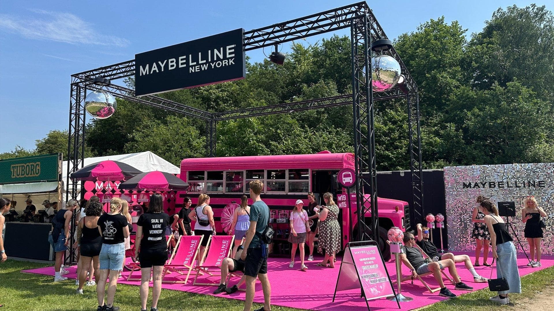 Vibrant pink pop-up scene med Maybelline-banner, mennesker og aktivitetsstationer udendørs