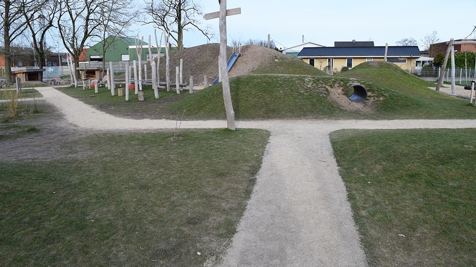 Kalkstenssti med græs og træer, gravkors og jordvold i baggrund