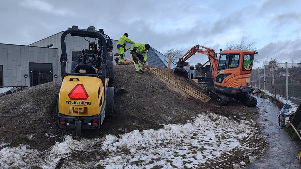 Arbejdskraft graver og transporterer jord til legebakke med kompactormaskine og minigraver