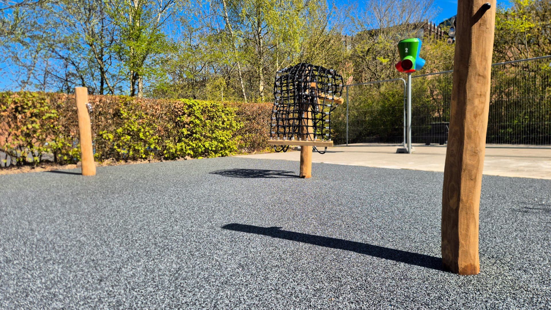 Legeplads med træstolper på gummifliser, grønt trafiksignal og naturhegn