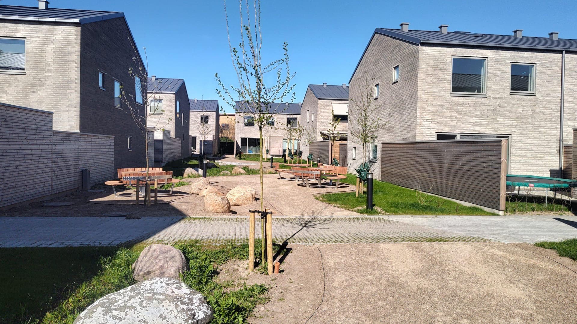 Boligområde med moderne huse omkring fælles legeplads med klatrestativ og grusvej