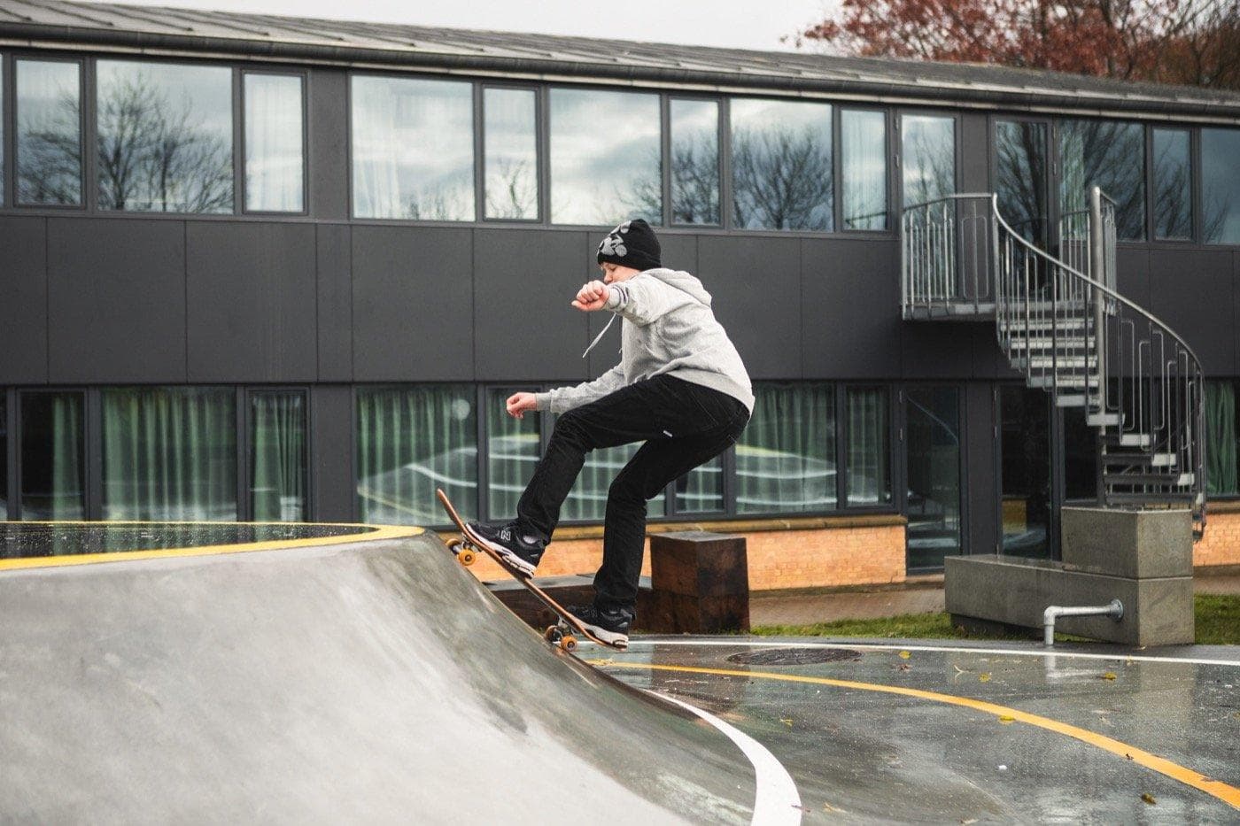 Person skaterborder over træ-feature på betonpark ved moderne bygning