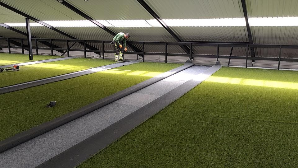 Indendørs kunstgræsanlæg med grå gangsystem mellem græsfelter under tagkonstruktion
