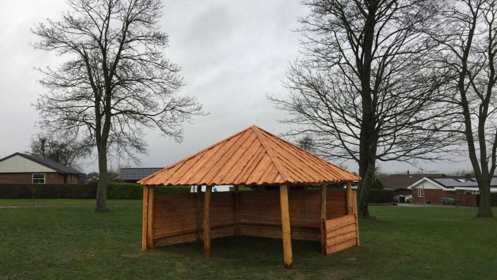 Ottekantet træpavillon med kobberbelagt tag på grønt græsareal mellem træer