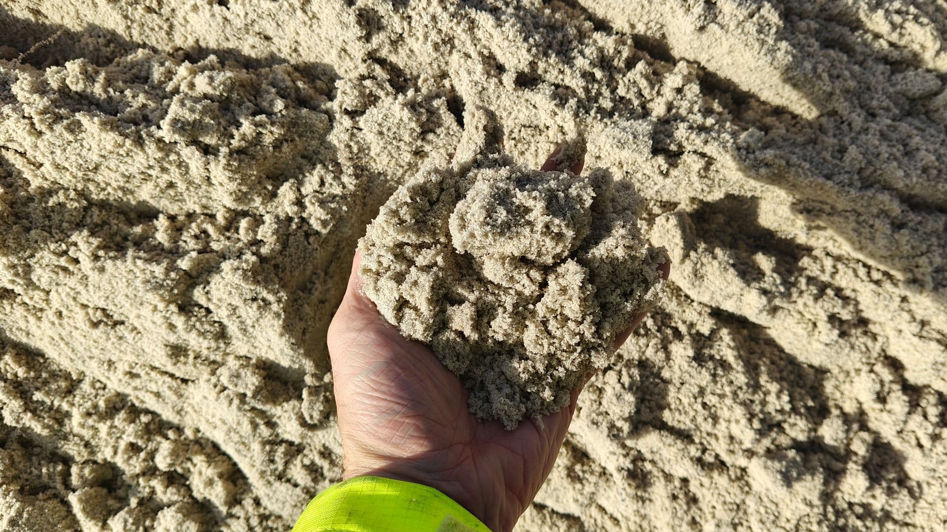 Hånd med en håndfuld fint, let fugtigt sand foran bunken, det er taget fra