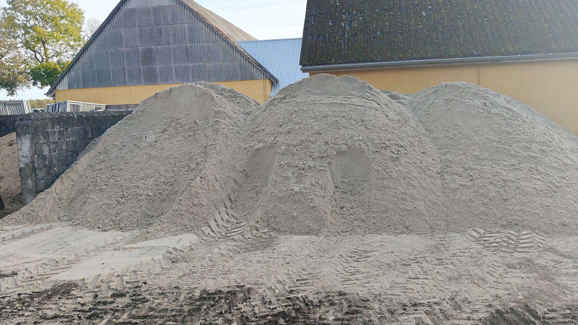 Tre store bunker lyst, fint sand på en gårdsplads foran gule bygninger